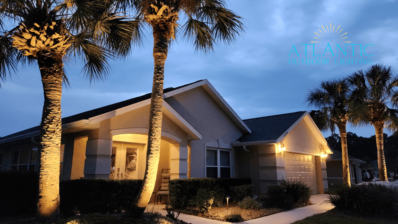 A house with a lit-up walkway and lit-up palm trees. Lightscaped by Atlantic Outdoor Lighting.